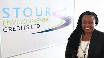 Black woman wearing black jacket over white top stood next to company sign